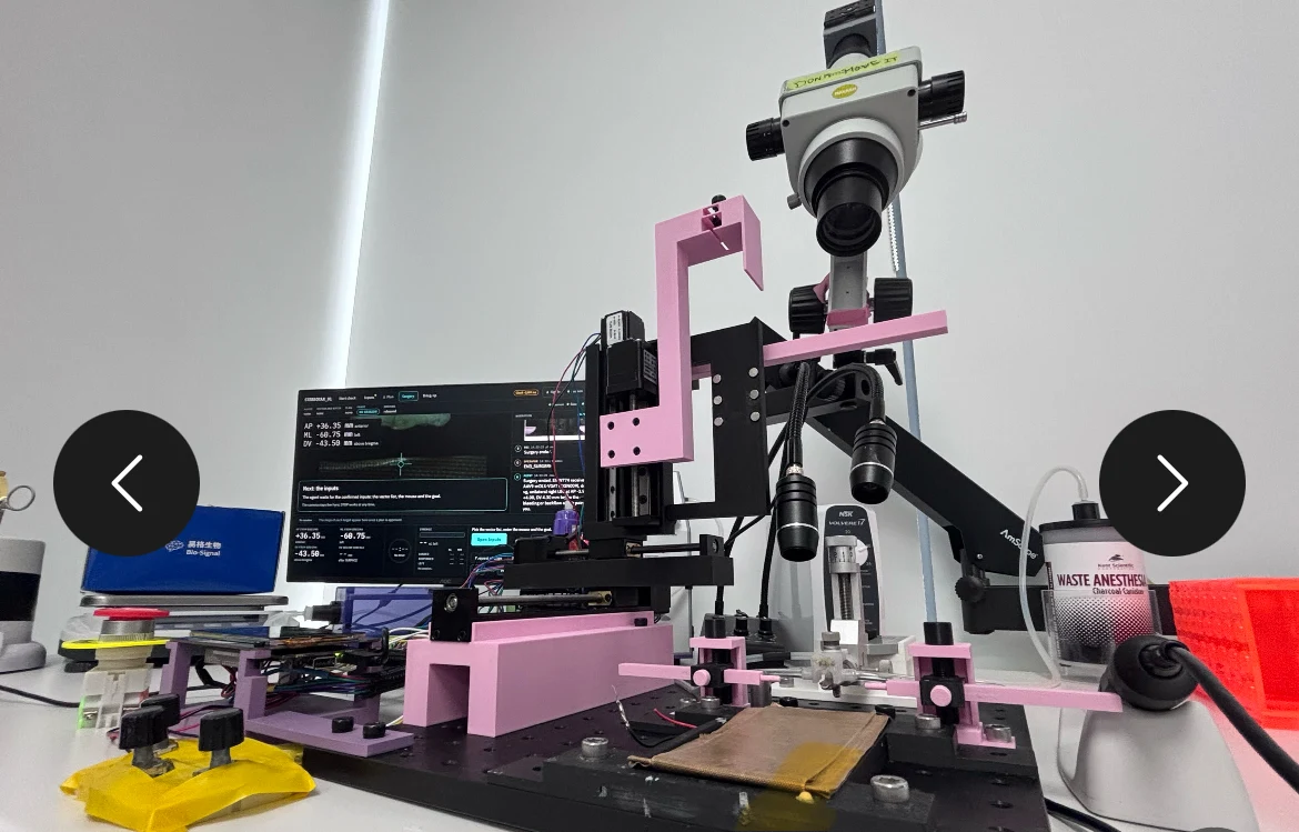 A motorized laboratory device with a microscope, monitor, and syringe.
