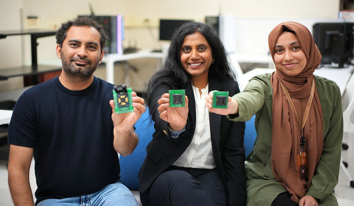 Three people seated in a lab hold up small green circuit boards.